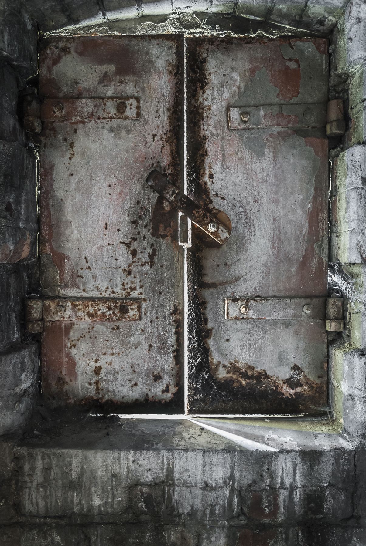 A rusted metal double-door in a warehouse, with sunlight from outside peaking through.