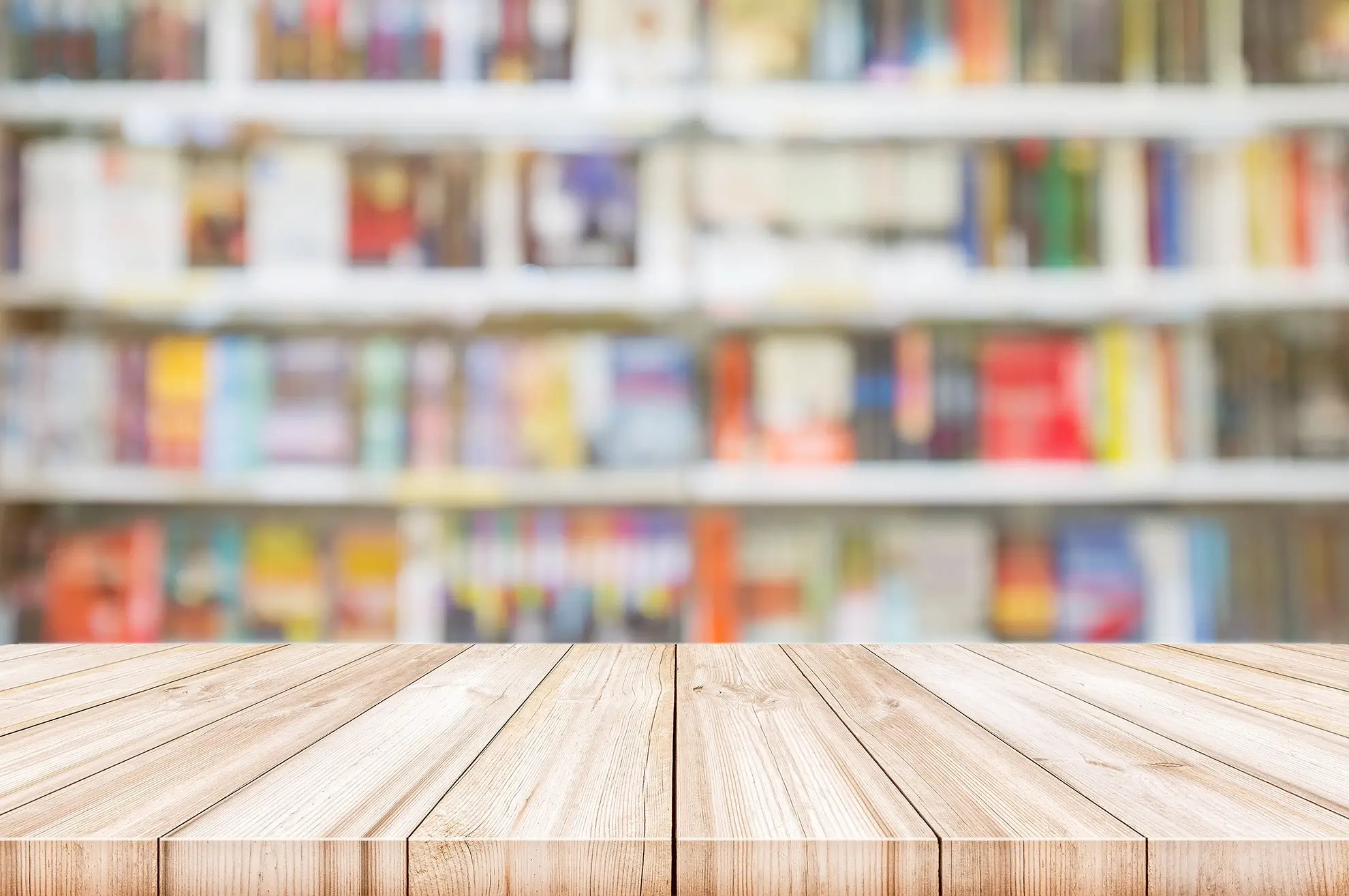 Image of a light wood table set in perspective in the foreground, with a blurred bookshelf in the background.